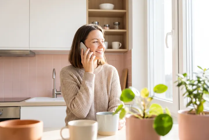 A relieved homeowner calling a plumber from her kitchen